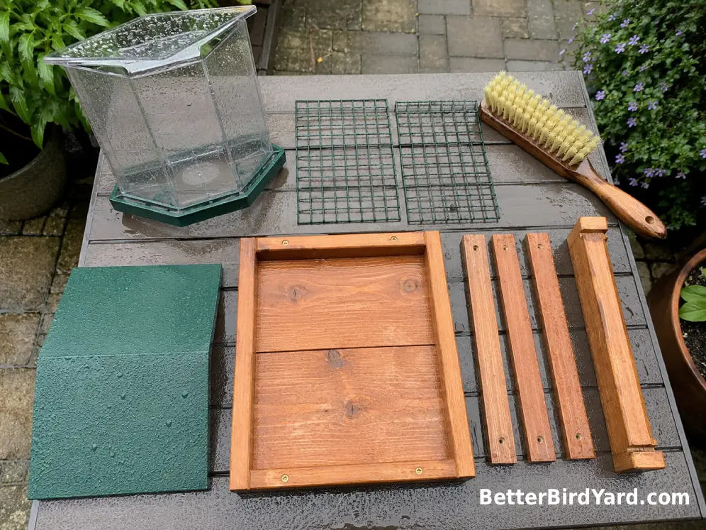 A disassembled platform bird feeder dries beside a scrub brush after cleaning.