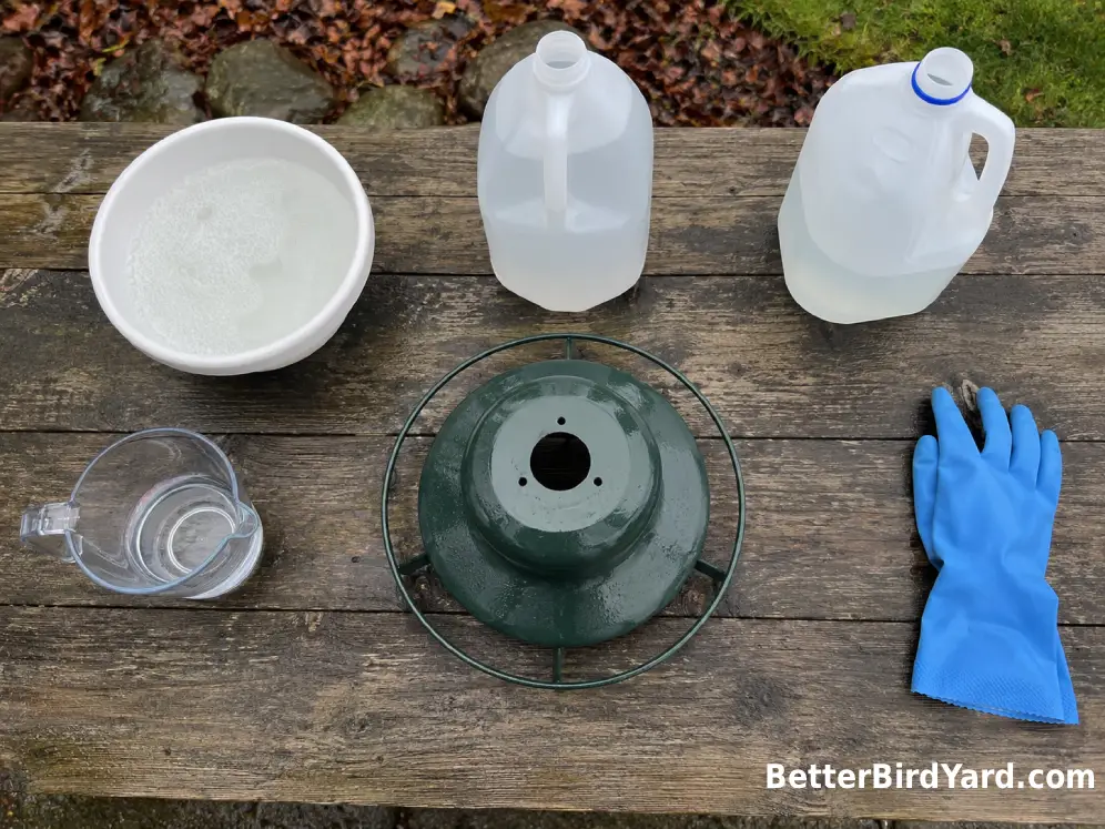 Three plain containers for soap, vinegar, and diluted bleach sit beside a clean feeder and measuring cup.