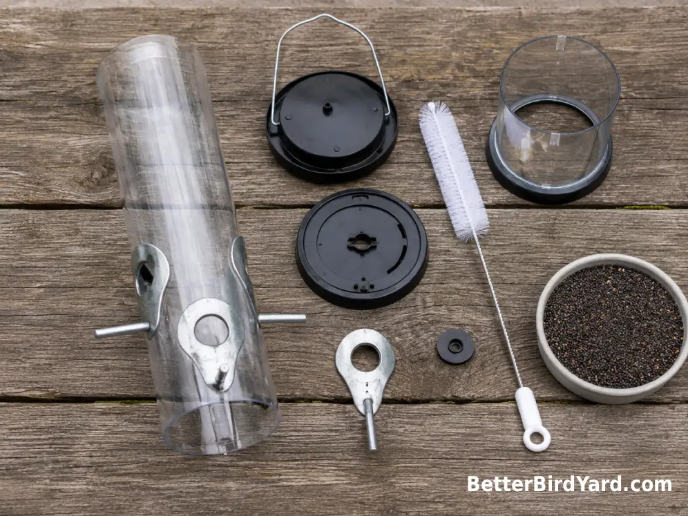 A disassembled finch feeder, cleaning brush, and fresh seed sit on an outdoor work surface.